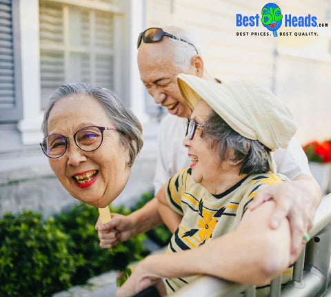 An elderly couple joyfully celebrating a simple anniversary, holding a face cutout with big smiles, adding a playful and heartwarming touch to their special day.