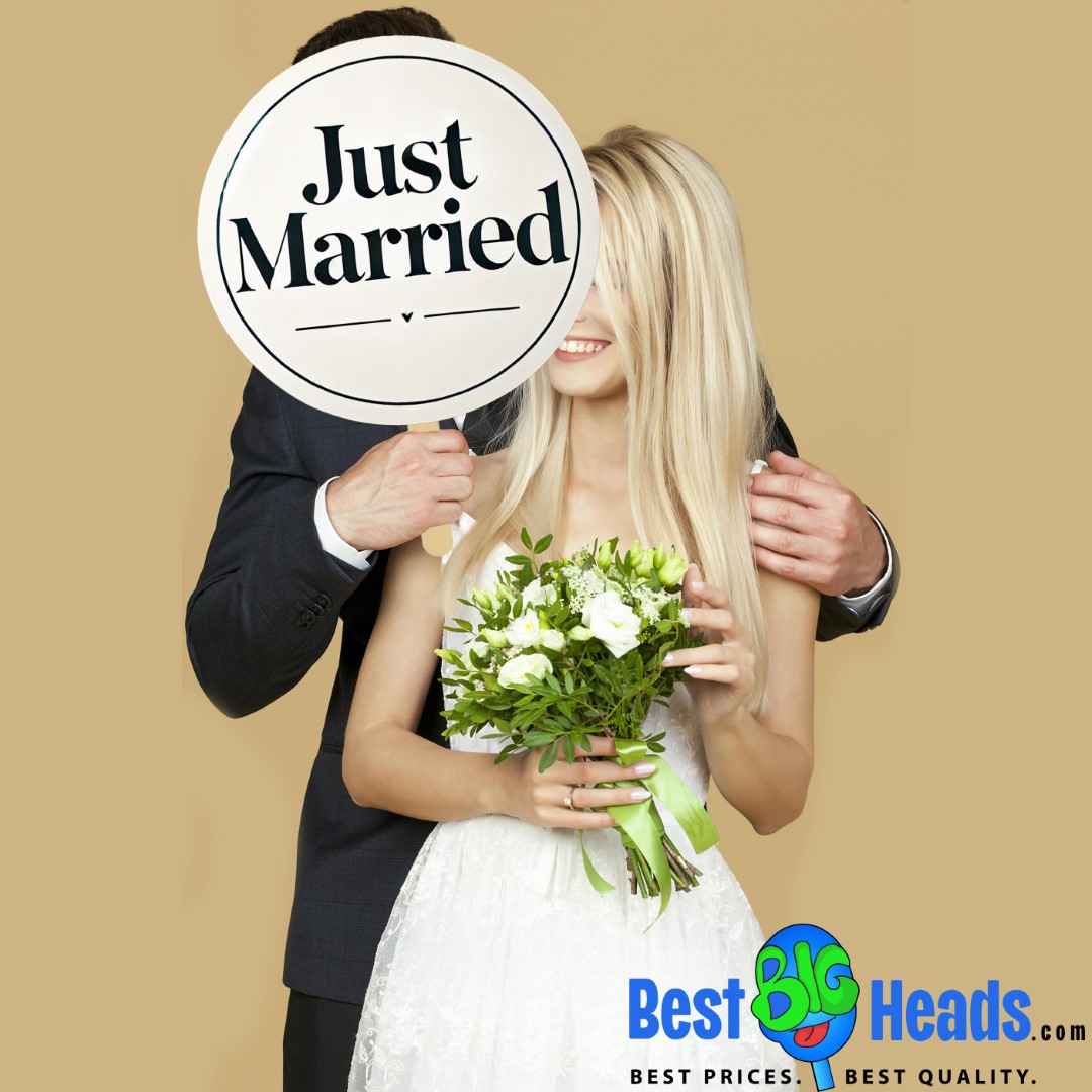 A newlywed couple holding a large "Just Married" sign that covers their faces. The bride is holding a bouquet of flowers, and both are smiling in front of a beige background.